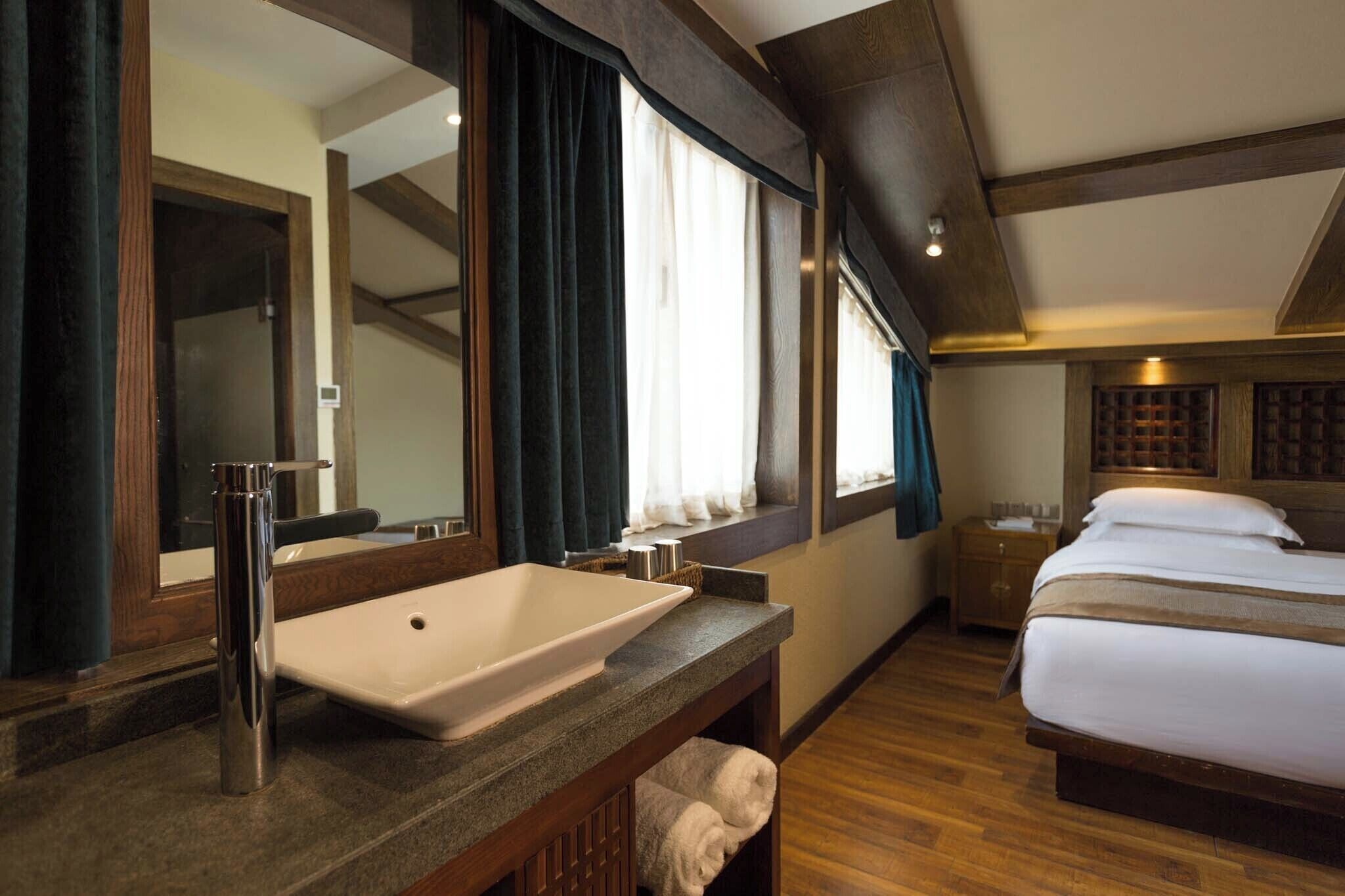 Een hotelkamer met een groot bed, een badkamer met wastafel en spiegel, en een raam met gordijnen.