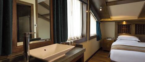 Een hotelkamer met een groot bed, een badkamer met wastafel en spiegel, en een raam met gordijnen.