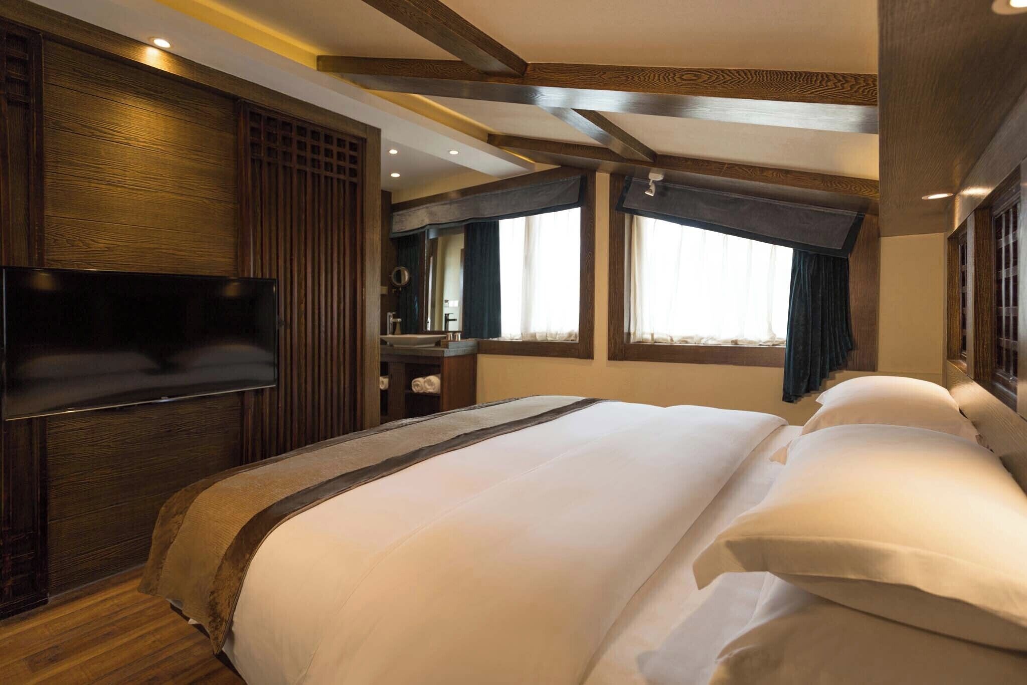 A hotel room with a large bed, wooden paneling, a flat-screen TV, a vanity with a mirror, and a window with curtains.