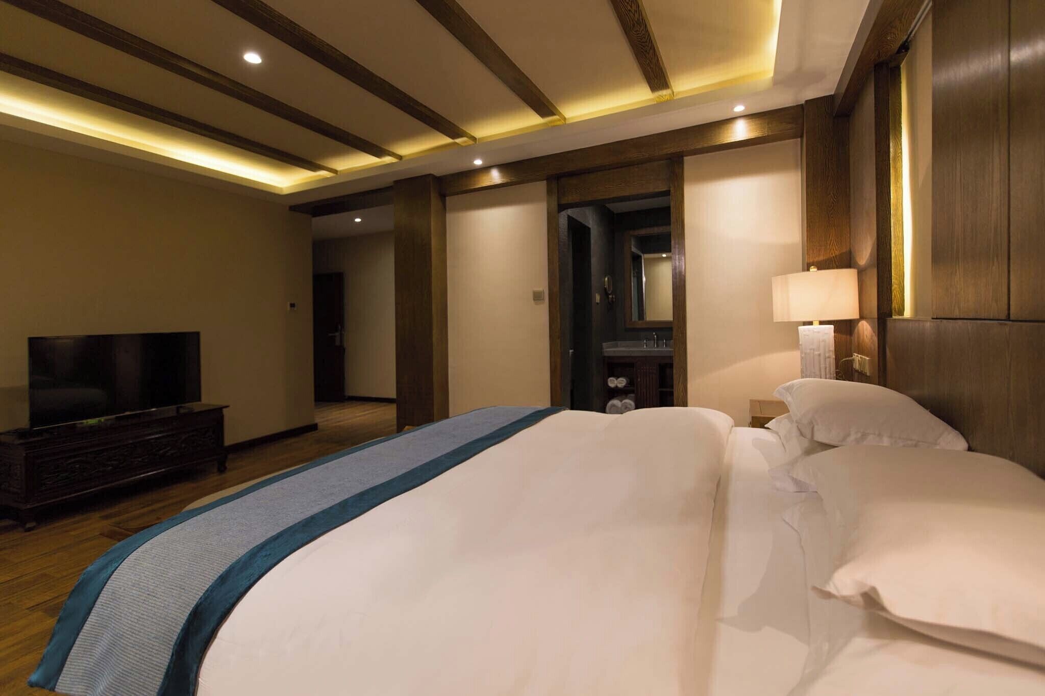 A hotel room with a bed, a TV, a bedside table, and a lamp.
