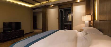 A hotel room with a bed, a TV, a bedside table, and a lamp.