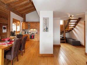 A modern kitchen with wooden cabinets, a dining area with chairs, and a staircase leading to a loft.