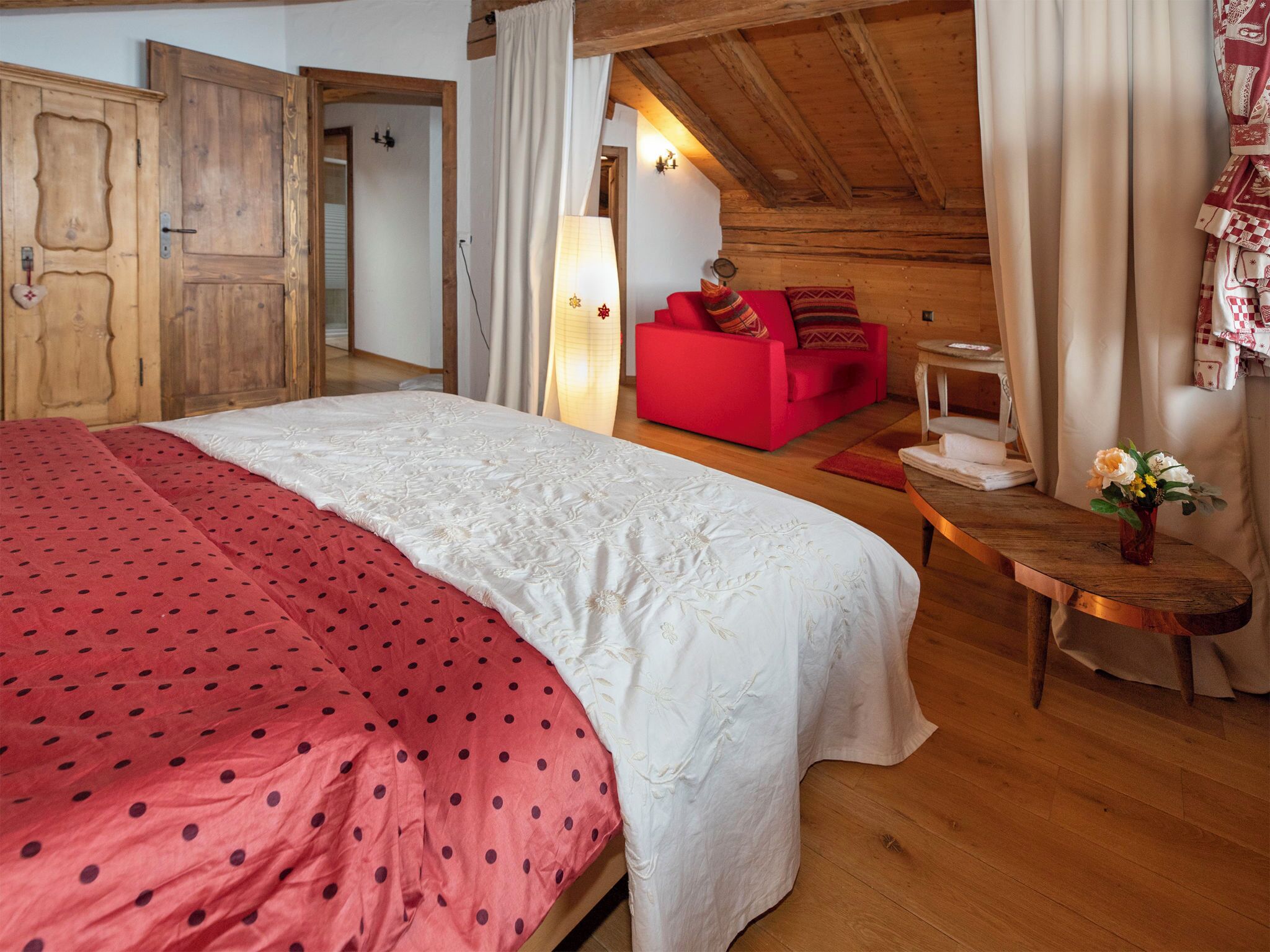 Une chambre avec un grand lit, un canapé rouge, une table en bois et une lampe.