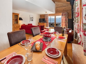A dining area with a wooden table set for four, red tablecloths, and a view of the outdoors through large windows.