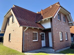 A two-story brick house with a red-tiled roof, a front door, and a small porch. - Ferienhaus in Burhave (Butjadingen)