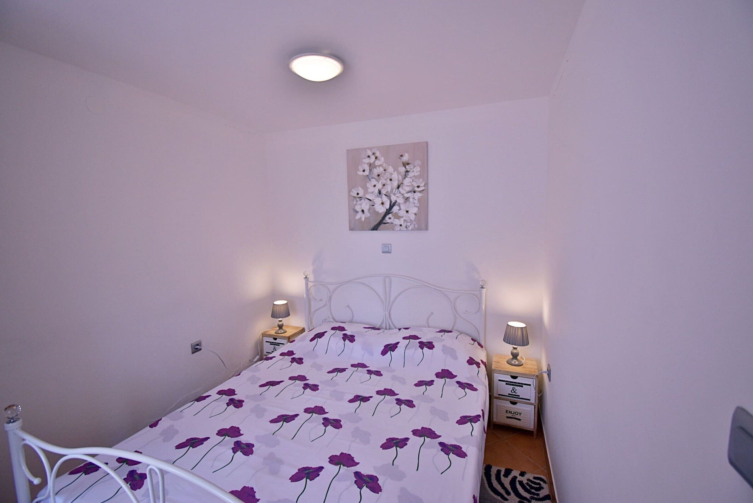 A single bed with a floral bedspread, two bedside tables with lamps, a wall-mounted picture, and a ceiling light.