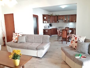 A living room with a sofa, a coffee table with flowers, and a dining area with chairs and a table. - Apartment in Pula Near Golf Course (Pula)