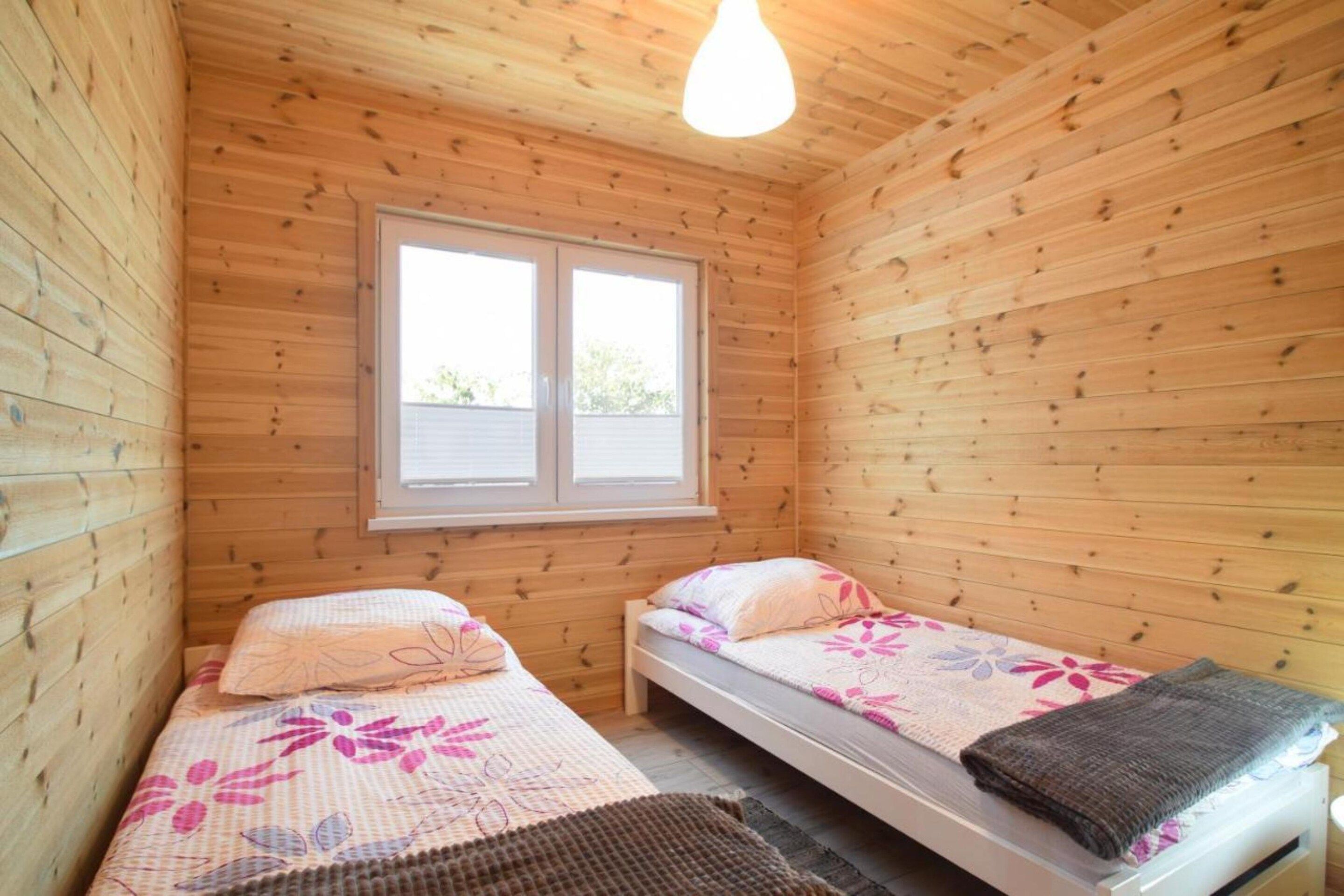 Eine kleine Holzhütte mit zwei Einzelbetten, einem Fenster und einer Lampe.