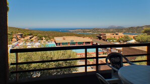 A balcony with a view of a pool, buildings, and a distant coastline. - Family Apartment in Olbia Near sea (Olbia)