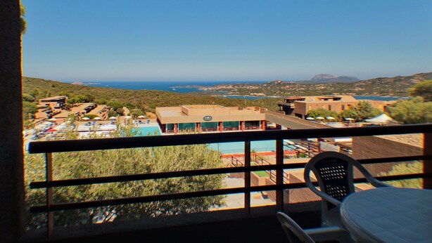 A balcony with a view of a pool, buildings, and a distant coastline. - Family Apartment in Olbia Near sea (Olbia)