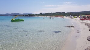 A beach with clear water, a green inflatable boat, and beach umbrellas. - Family Apartment in Olbia Near sea (Olbia)
