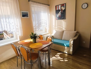 A living room with a wooden dining table, chairs, a sofa, a potted plant, and a painting on the wall. - Apartment in Miedzyzdroje Near the Beach (Międzyzdroje)