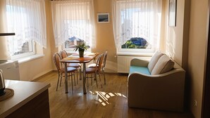 Ein gemütliches Wohnzimmer mit Essbereich, Holzboden, einer Couch und Blick durch die Fenster.