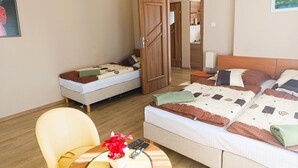 Ein Hotelzimmer mit zwei Betten, einem Sessel, einem kleinen Tisch mit Pflanze und Fernbedienungen sowie einem Holzschrank.