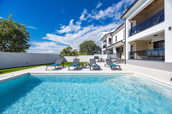 A modern pool area with lounge chairs, a clear blue pool, and a two-story building with large windows. - Villa in Pula Near Hidrobaza Beach (Pula)