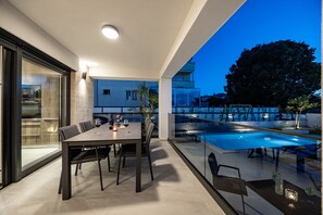 A modern outdoor dining area with a pool, glass railings, and a view of the cityscape at dusk. - Villa in Pula Near Hidrobaza Beach (Pula)
