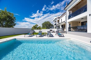 A modern pool area with a clear blue pool, lounge chairs, and a two-story building with large windows. - Villa in Pula Near Hidrobaza Beach (Pula)