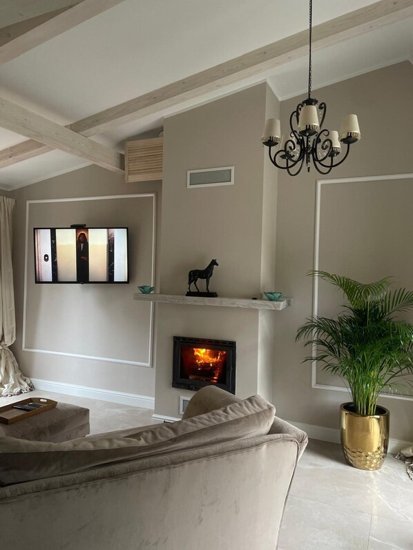 A living room with a fireplace, a sofa, a television, and a chandelier. - Holiday Home With Sauna and Whirlpool (Międzyzdroje)