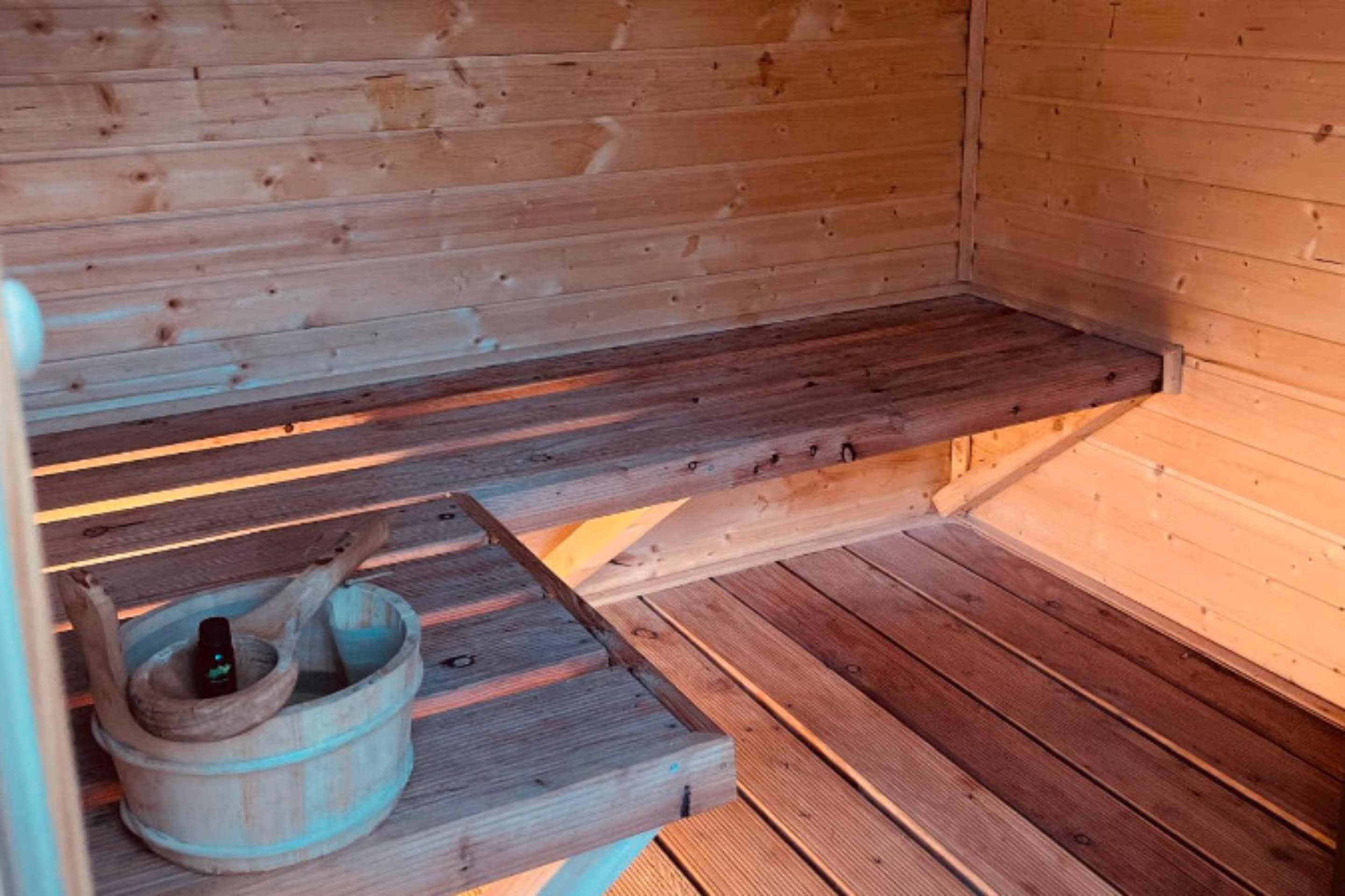 Un banc en bois pour sauna, accompagné d’un seau en bois et d’un maillet en bois.