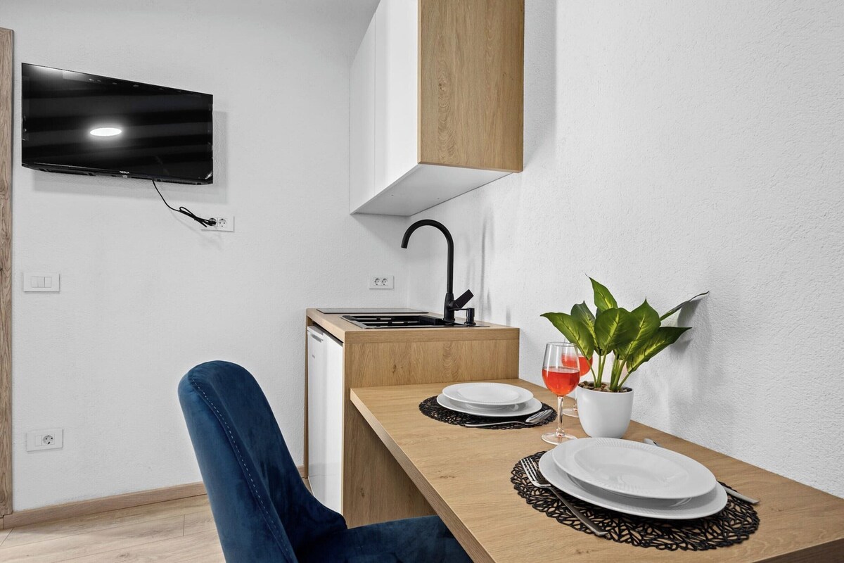 Eine moderne Küche mit Flachbildfernseher, Holdekor-Schränken, einer Spüle und einer Essecke mit Tisch für zwei Personen.
