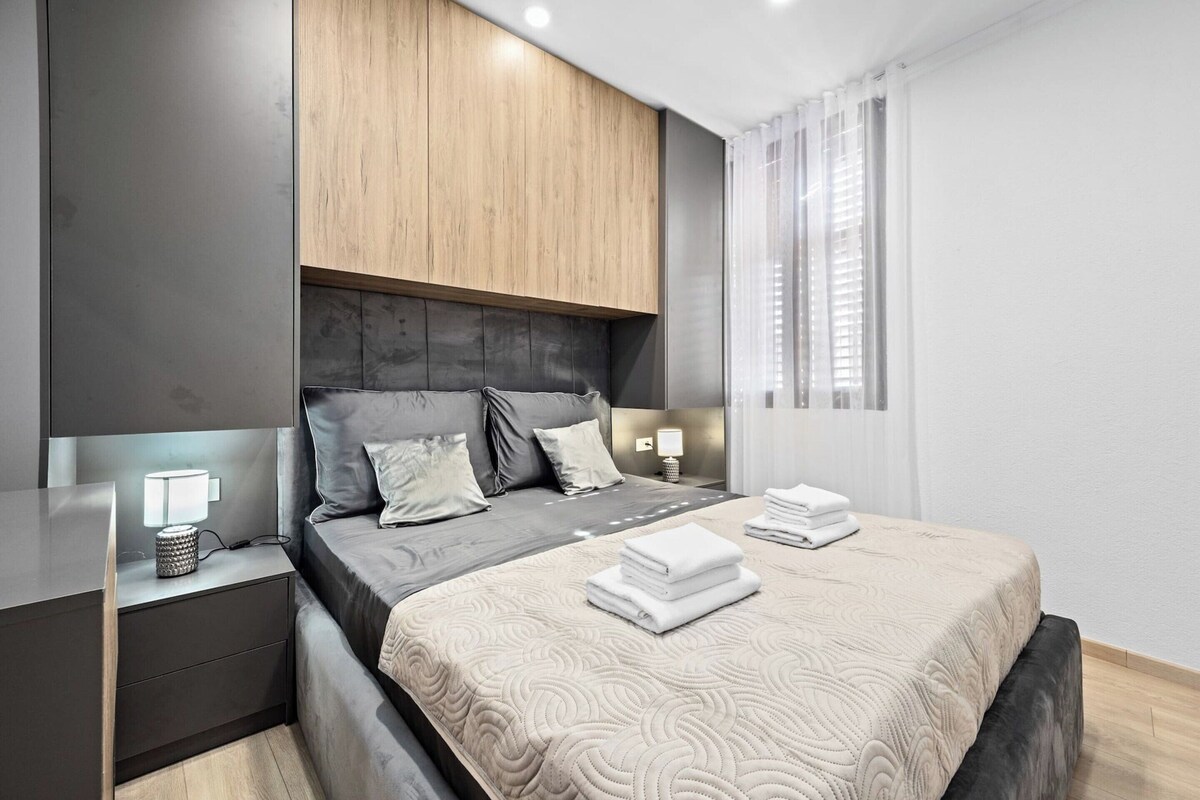 Ein modernes Schlafzimmer mit Bett, Nachttischen und einem Fenster mit Vorhängen.