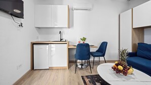 En kompakt opholdsstue med tekøkken, spiseplads og siddeområde med sofa og stole.