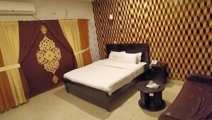 A hotel room with a bed, a small round table, a chair, and a decorative wall panel. - Rooms Near Centurus Mall islamabad (Islamabad)