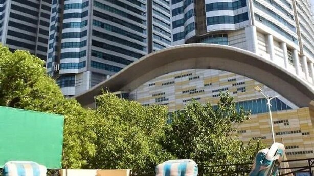 A high-rise building with a curved structure in the foreground, surrounded by greenery. - Rooms Near Centurus Mall islamabad (Islamabad)