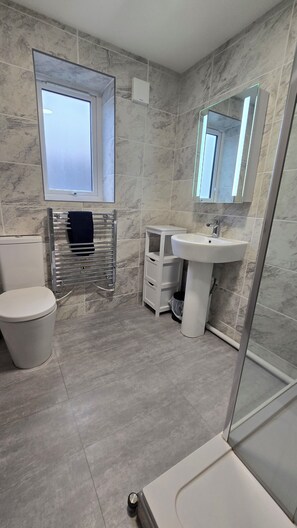 A modern bathroom with a toilet, a sink, a mirror, and a shower. - Menai View Apartment (Y Felinheli)