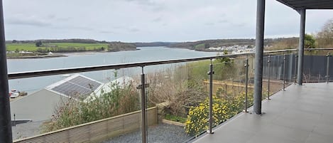 Un espacio al aire libre techado con vistas a un cuerpo de agua, un área verde y un edificio con paneles solares.