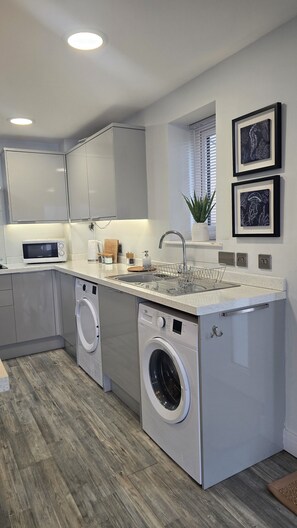 A modern kitchen with built-in appliances, a sink, and a washing machine. - Menai View Apartment (Y Felinheli)