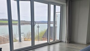 Ein Schlafzimmer mit großen Fenstern, einem Bett und Blick auf ein Gewässer.