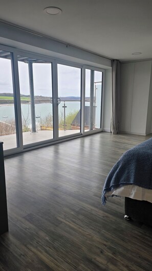 A bedroom with large windows, a bed, and a view of a body of water. - Menai View Apartment (Y Felinheli)