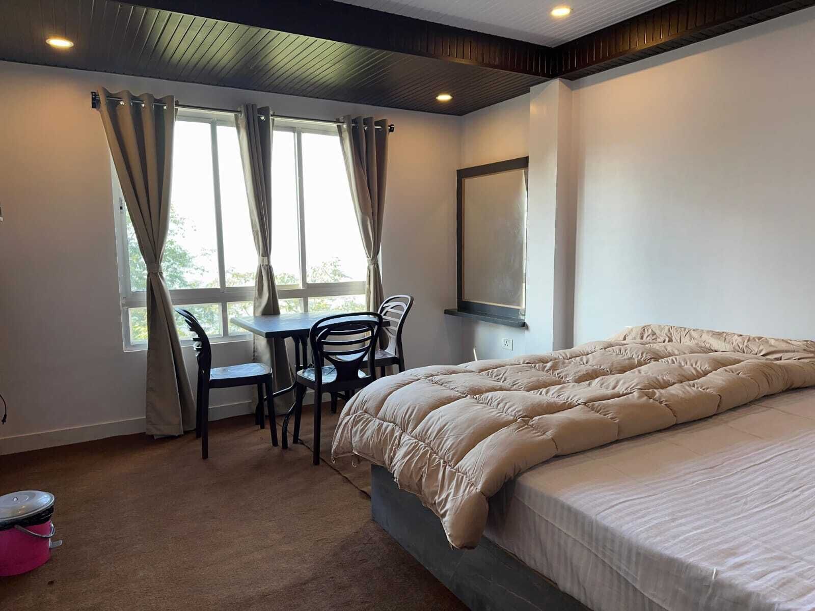 Een slaapkamer met een bed, een bureau, twee stoelen, een raam met gordijnen en een plafondlamp.
