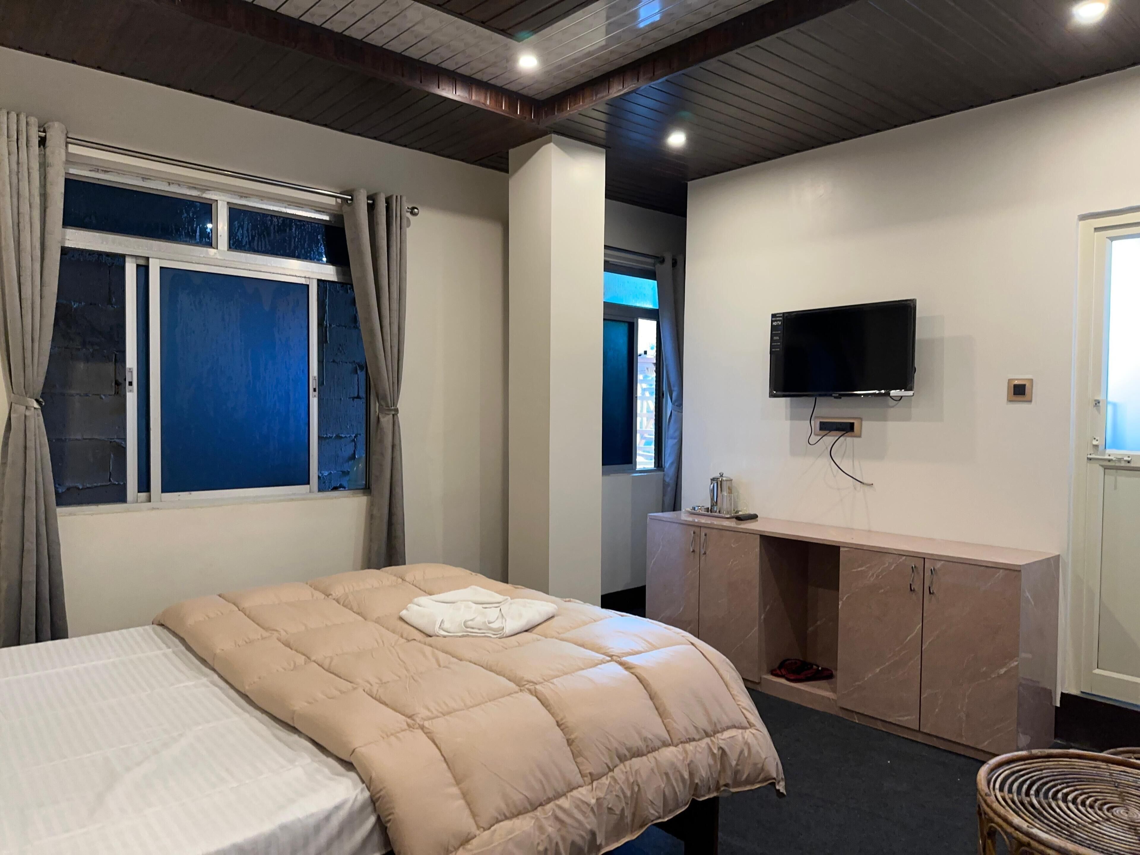 A bedroom with a bed, a TV, a desk, and a window with curtains.