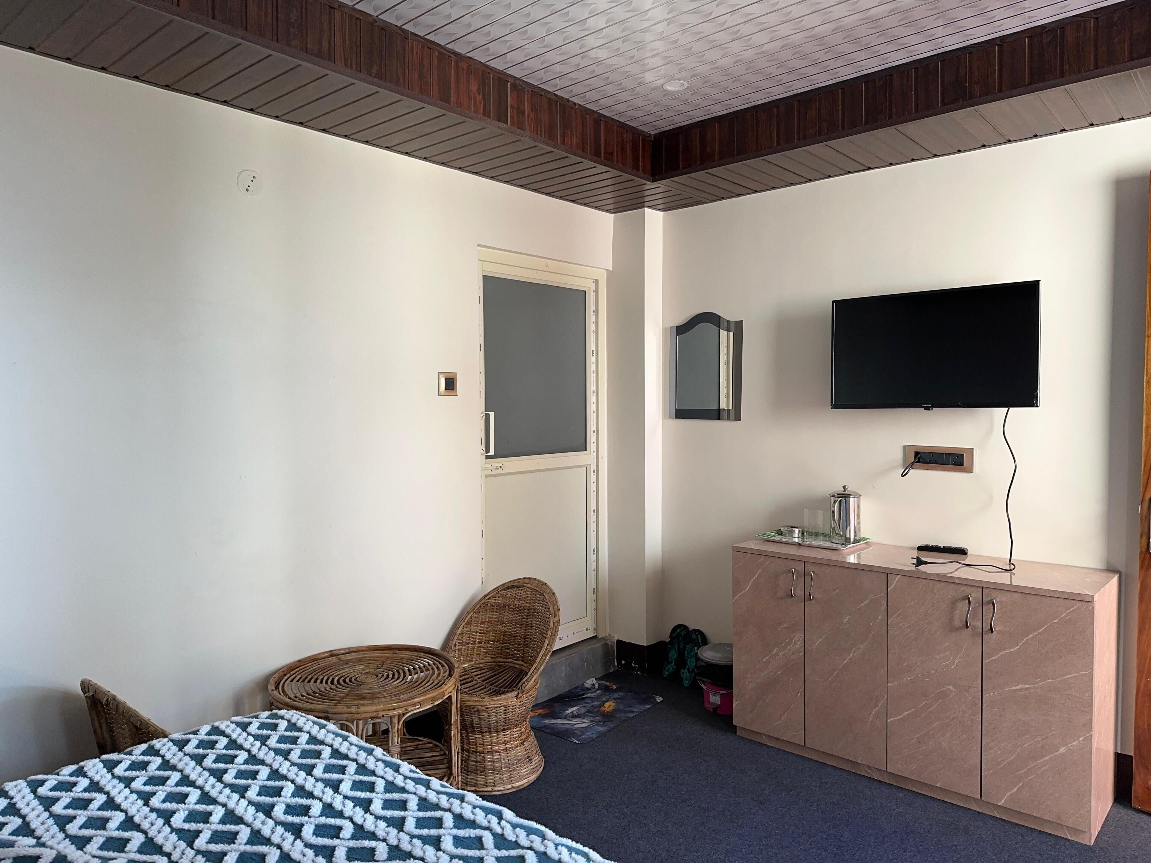 Una habitación de hotel con una cama, un televisor en la pared, una silla de mimbre, un armario y una puerta.