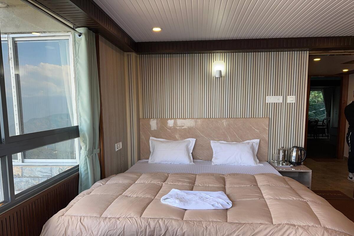 A hotel room with a large bed, a window, a wall-mounted lamp, and a view of the outdoors.