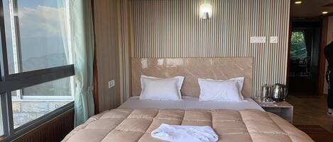 A hotel room with a large bed, a window, a wall-mounted lamp, and a view of the outdoors.