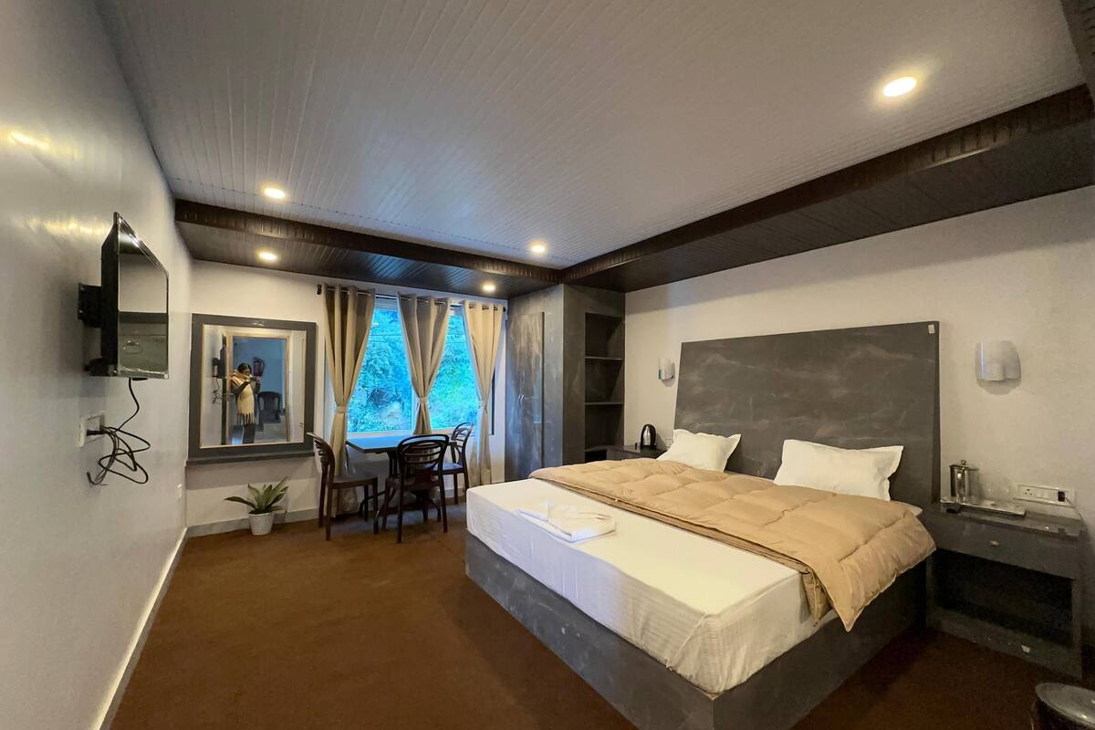 A modern hotel room with a large bed, a desk with chairs, a window with curtains, and a television mounted on the wall.