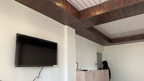 A room with a mounted television, a wooden ceiling, a wardrobe, and a door.