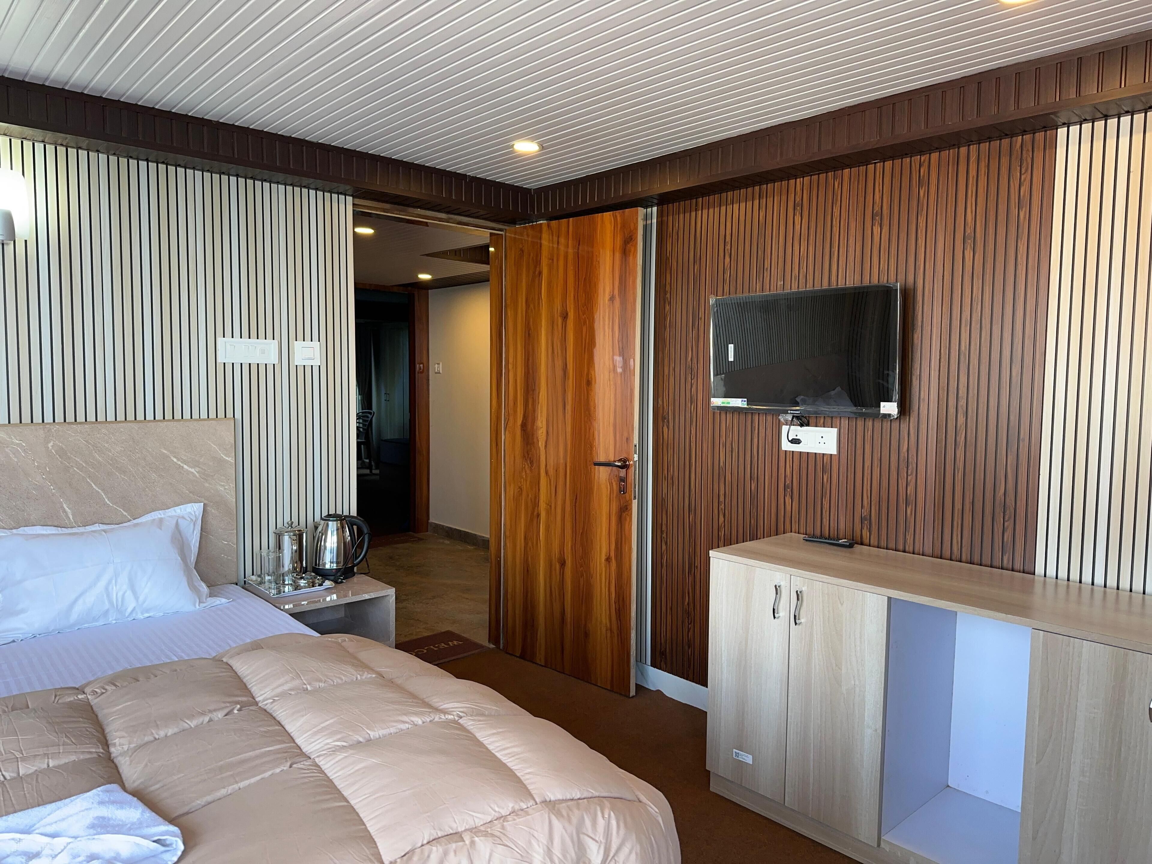 A modern hotel room with a bed, a TV mounted on the wall, a wooden cabinet, and a small table with a kettle.