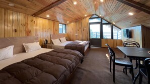 A cabin with wooden walls, a pitched roof, two beds, a table, and chairs.