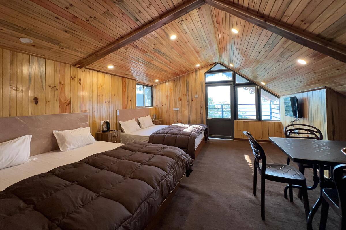 A cabin with wooden walls, a pitched roof, two beds, a table, and chairs.