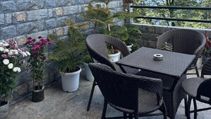 A balcony with a stone wall, wicker furniture, potted plants, and a clear view of trees and sky.