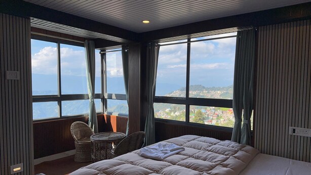 A bedroom with a large bed, a chair, and a view of a mountainous landscape through large windows.
