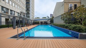 Una piscina con cubierta de madera, rodeada de edificios y vegetación.