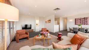 Una sala de estar moderna con sofá, sillón, televisor y un comedor con sillas y mesa.