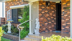 A brick building with a porch, a statue, a bird bath, and a 'Summer Wind' sign. - Summer Wind - Beachside Stay Near Kendalls Beach (Kiama)