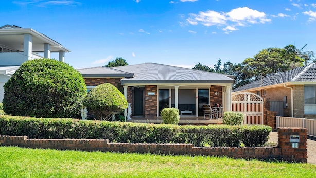 A two-story house with a covered porch, a brick exterior, and a well-maintained front yard. - Summer Wind - Beachside Stay Near Kendalls Beach (Kiama)