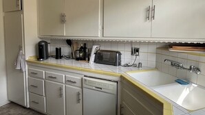 Ett kök med vita skåp, en gul köksbänk, en diskmaskin, en brödrost och ett handfat.